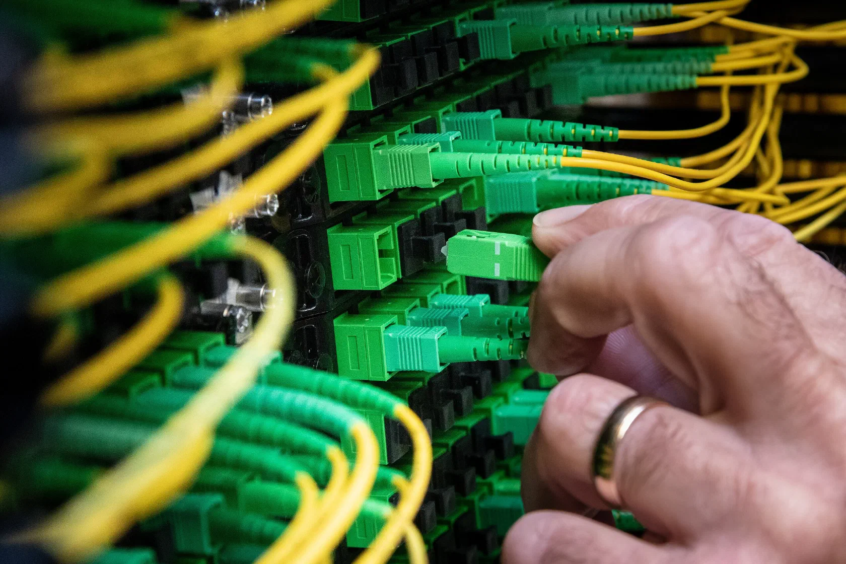 A technician patching green fibre-optic cables in a network rack